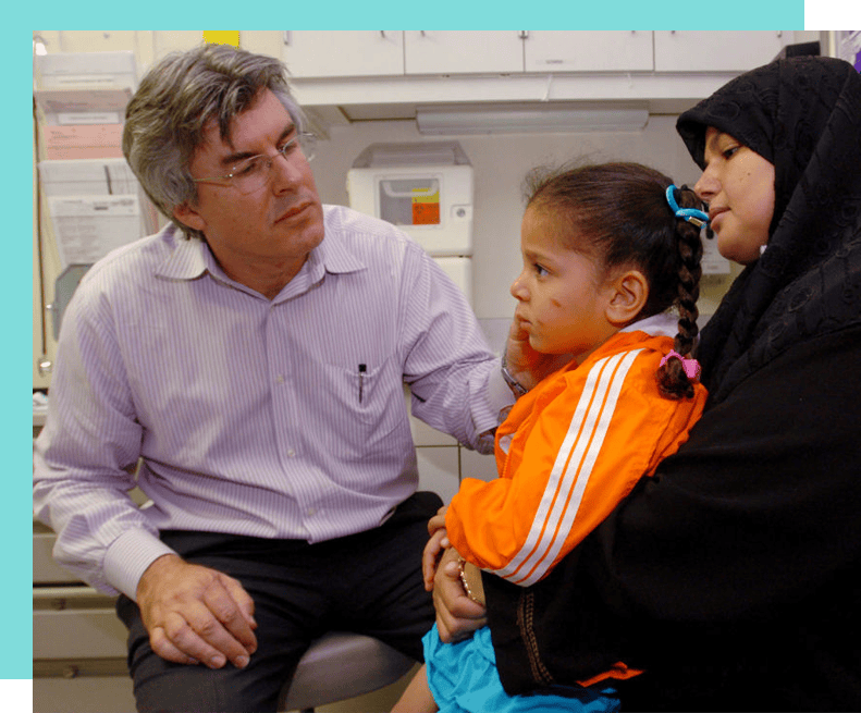 Dr. Canoun Examining Child Being Held By Her Mother With Turquoise Frame Behind Image